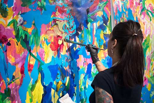 person painting a canvas in an abstract way with variety of bright colors: blue, green, yellow